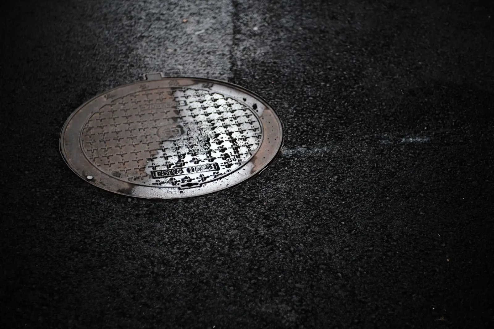 A cast iron drain cover set into wet tarmac