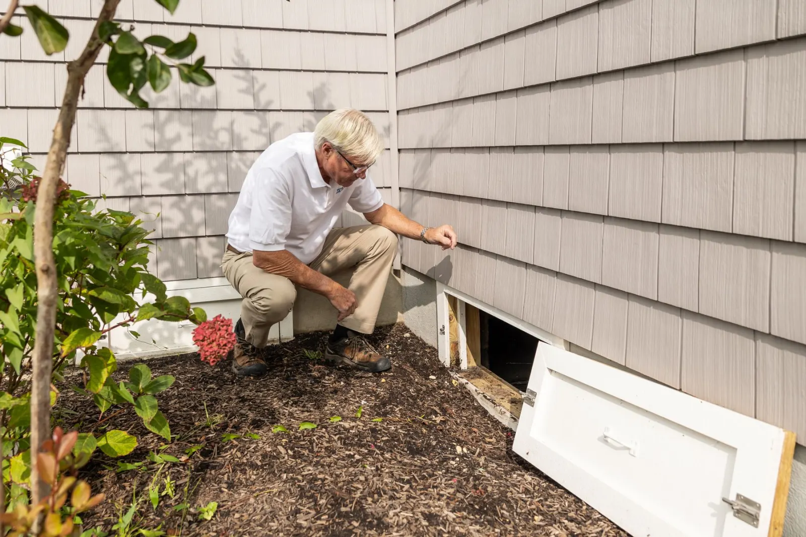 An engineer kneeling to work on a unit against a house wall